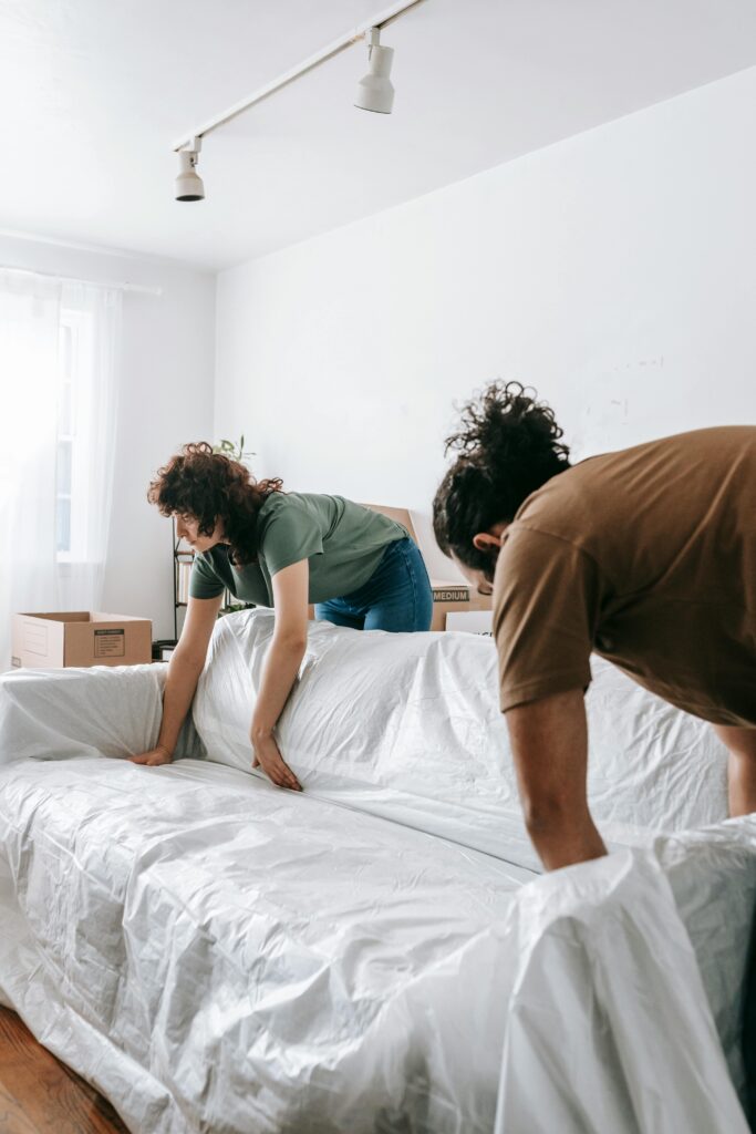 Current image: A couple packing their sofa for relocation by wrapping it in protective plastic.